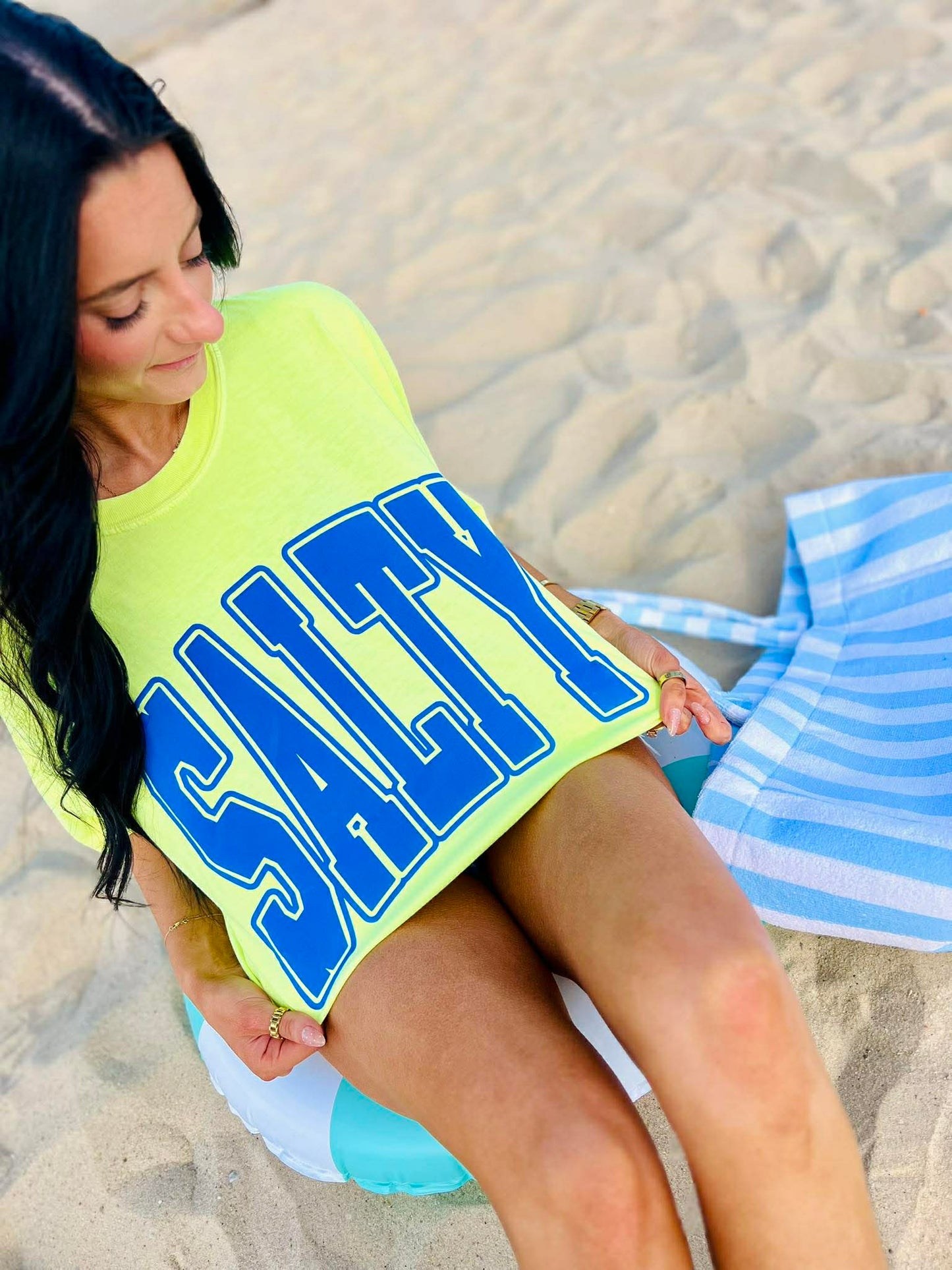 Woman on a beach wearing a bright yellow 'Salty' shirt.