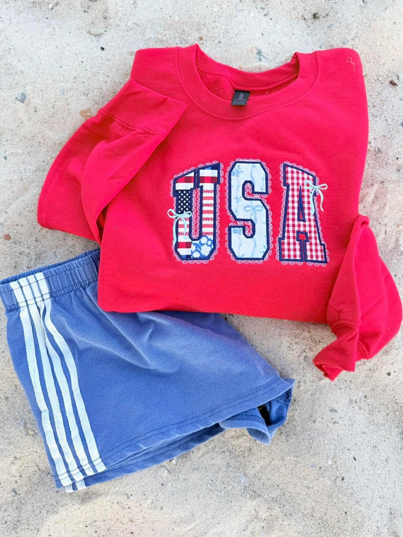 Red sweatshirt with 'USA' embroidery appliqué print and blue shorts on a Beach surface