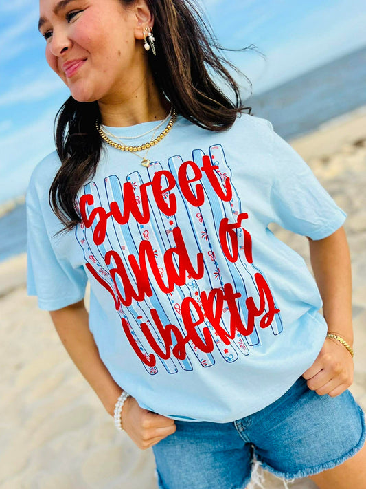 Woman wearing a light blue t-shirt with 'Sweet Land of Liberty' text on a beach.