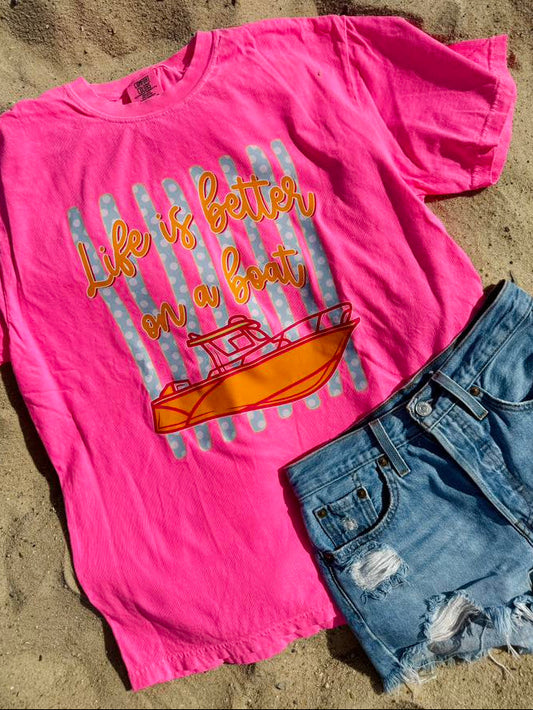 Pink t-shirt with 'Life is better on a boat' graphic and denim shorts on sand