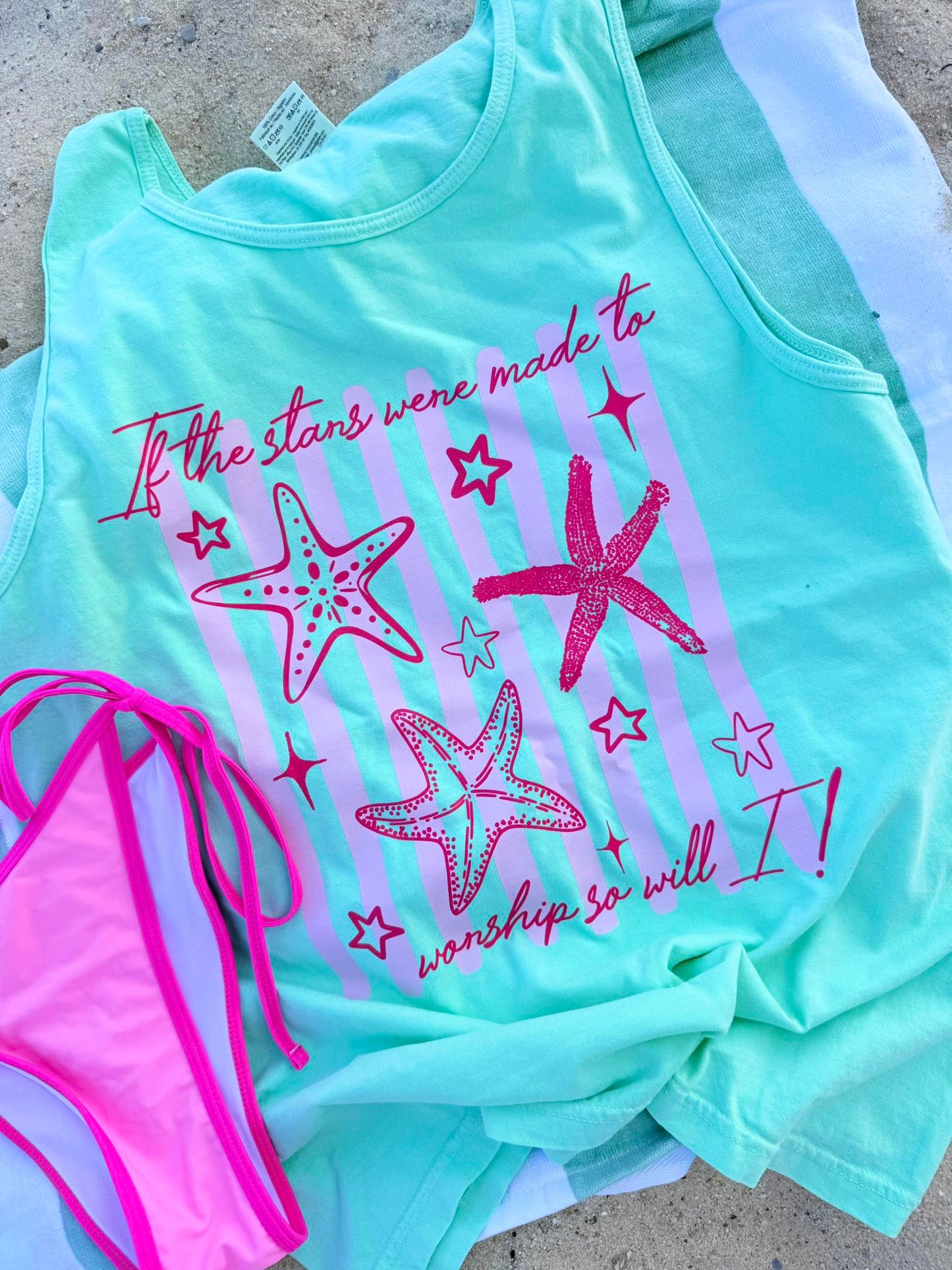 Mint green tank top with pink starfish design and text, paired with a pink bikini bottom on a concrete surface.