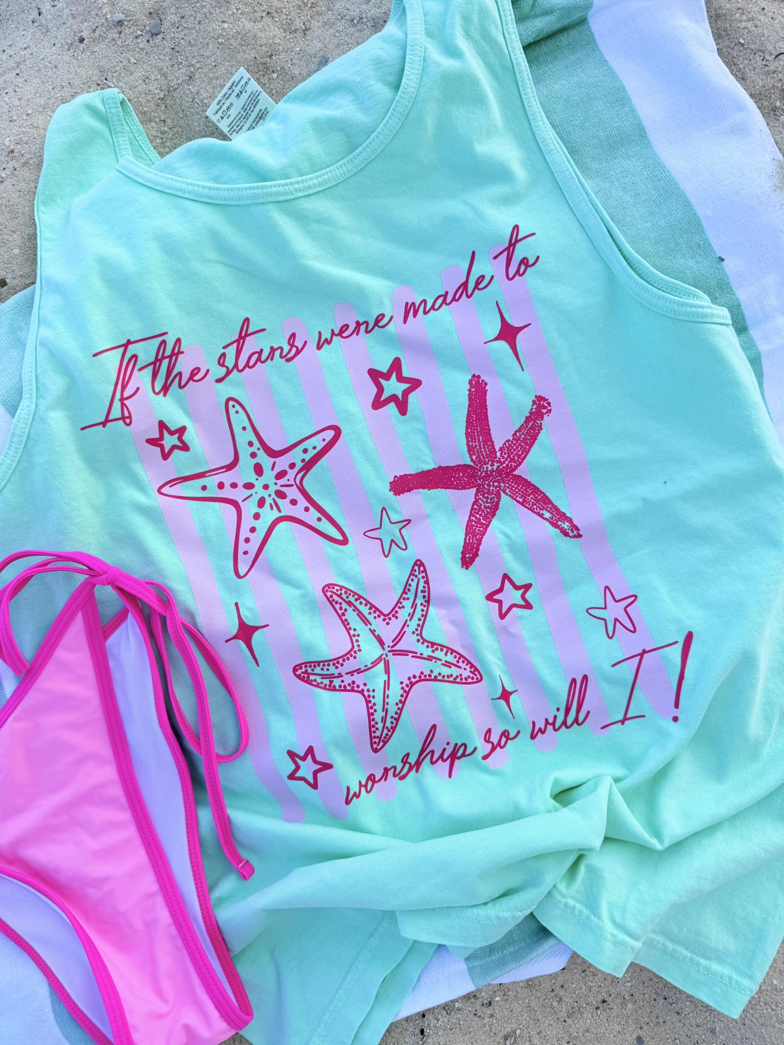 Mint green tank top with pink starfish design and text, paired with a pink bikini bottom on a concrete surface.