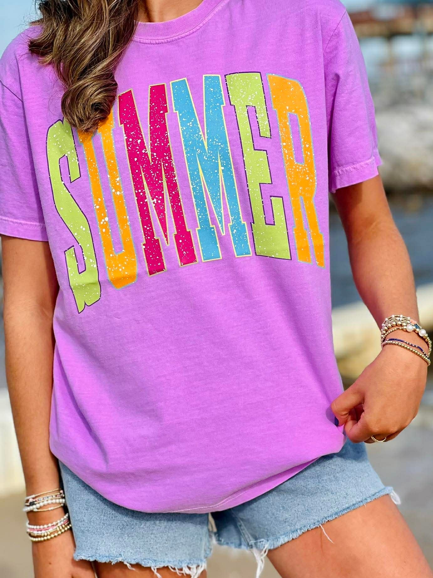 Person wearing a purple t-shirt with 'SUMMER' in colorful letters, standing outdoors.
