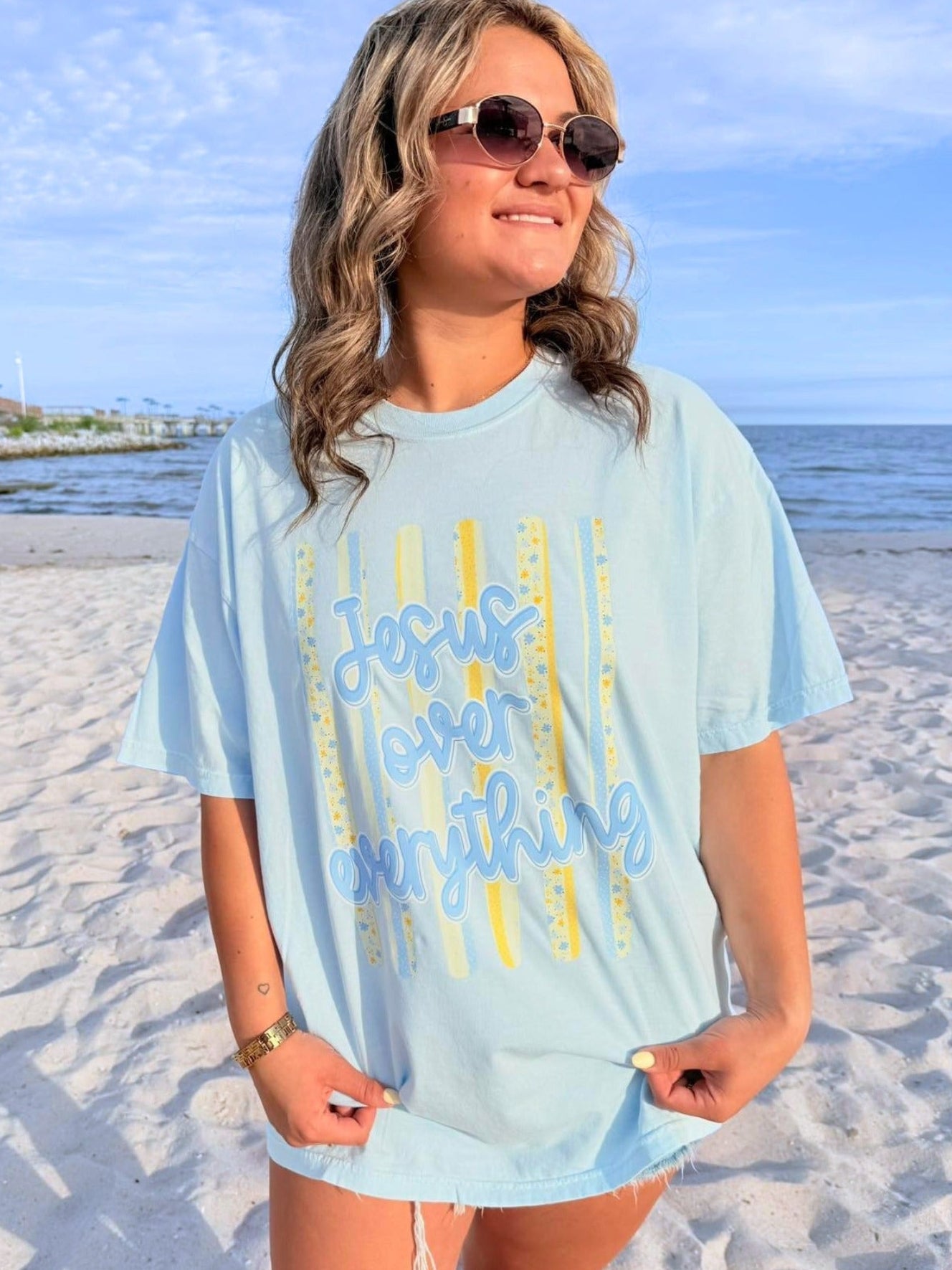 Woman wearing a light blue t-shirt with yellow graphics "Jesus over everything" on a beach