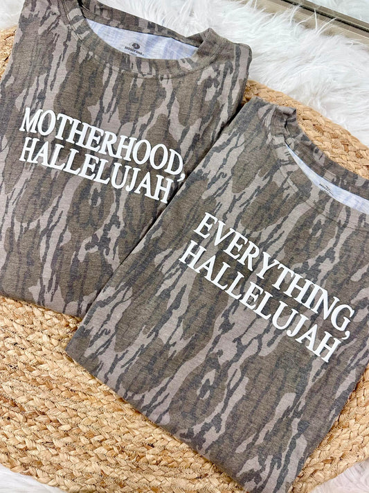 Two camouflage-patterned shirts with Motherhood, Hallelujah and Everything, Hallelujah puff text on a Bottomland surface