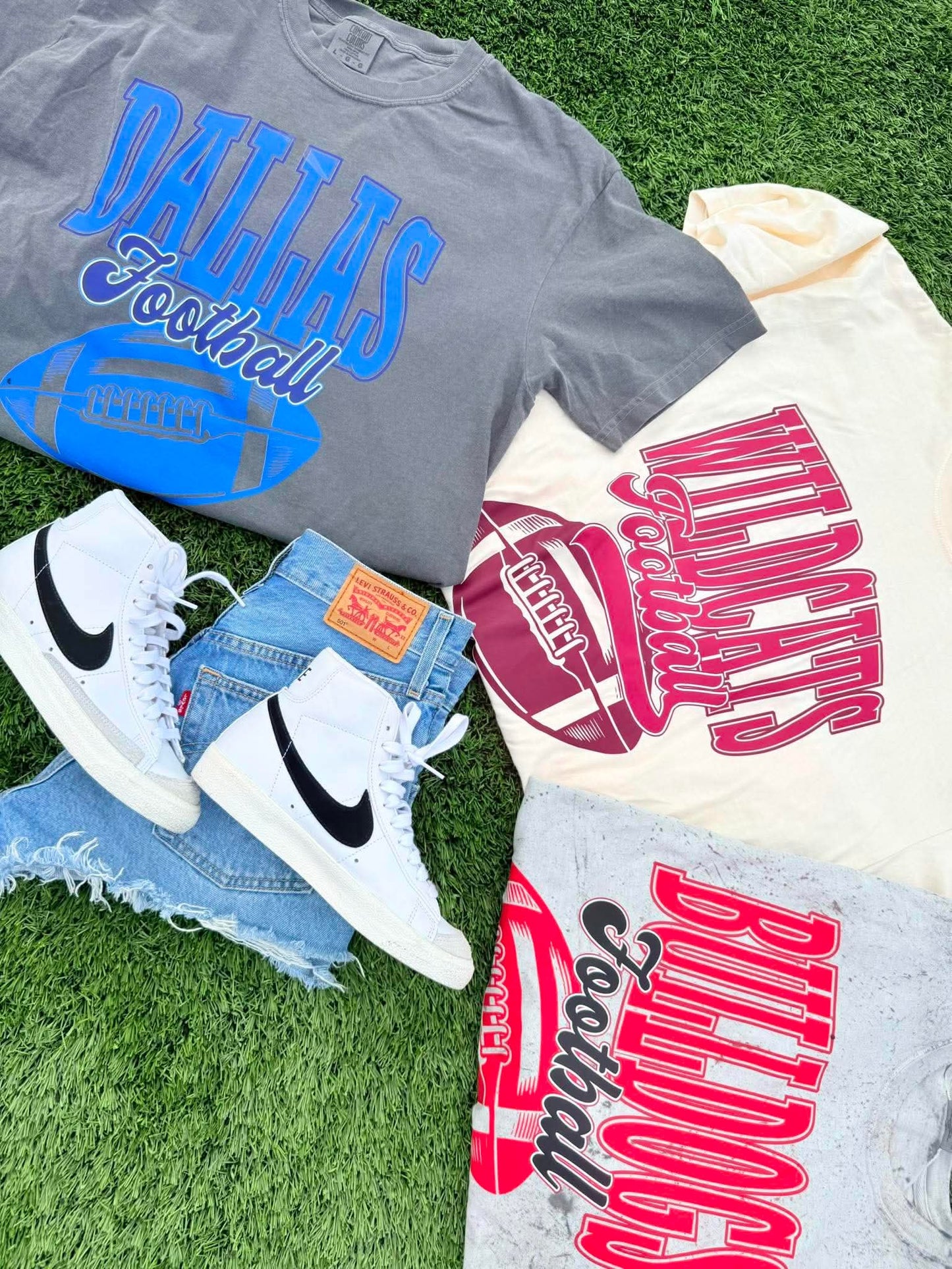 Gray t-shirt with 'Dallas Football' text, white sneakers, and denim shorts on grass.
