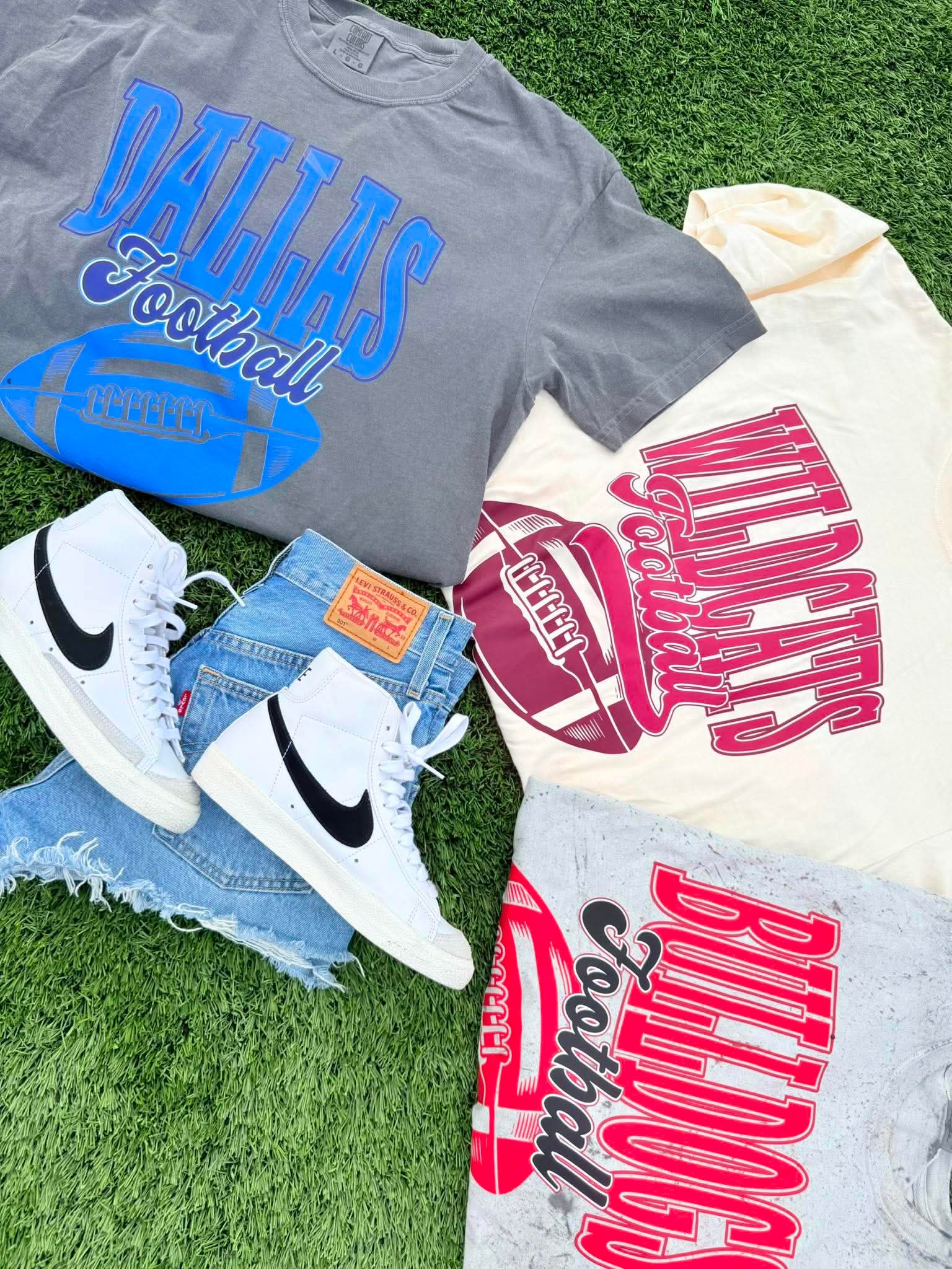 Gray t-shirt with 'Dallas Football' text, white sneakers, and denim shorts on grass.