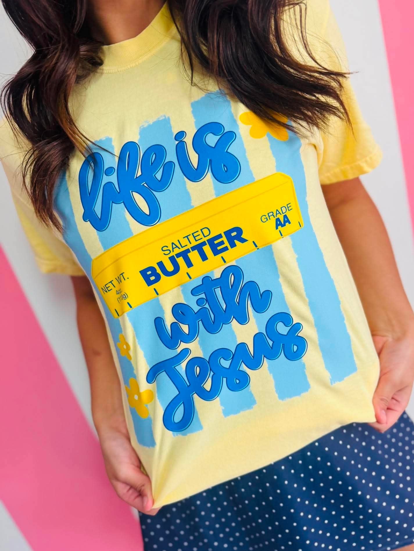 Person wearing a yellow t-shirt with blue text on a pink and white striped background