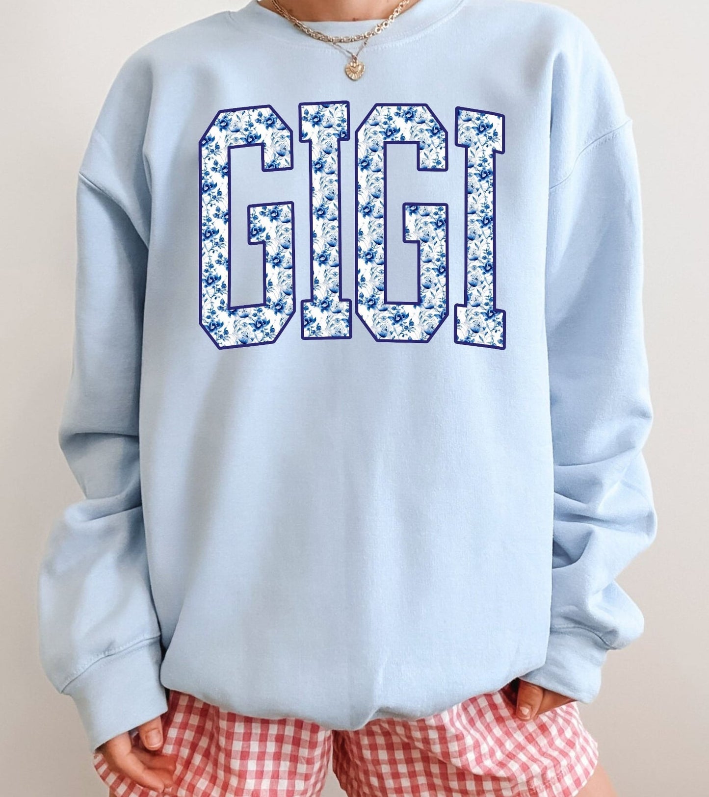 Light blue sweatshirt with 'GIGI' printed on it, worn by a person with red checkered shorts.