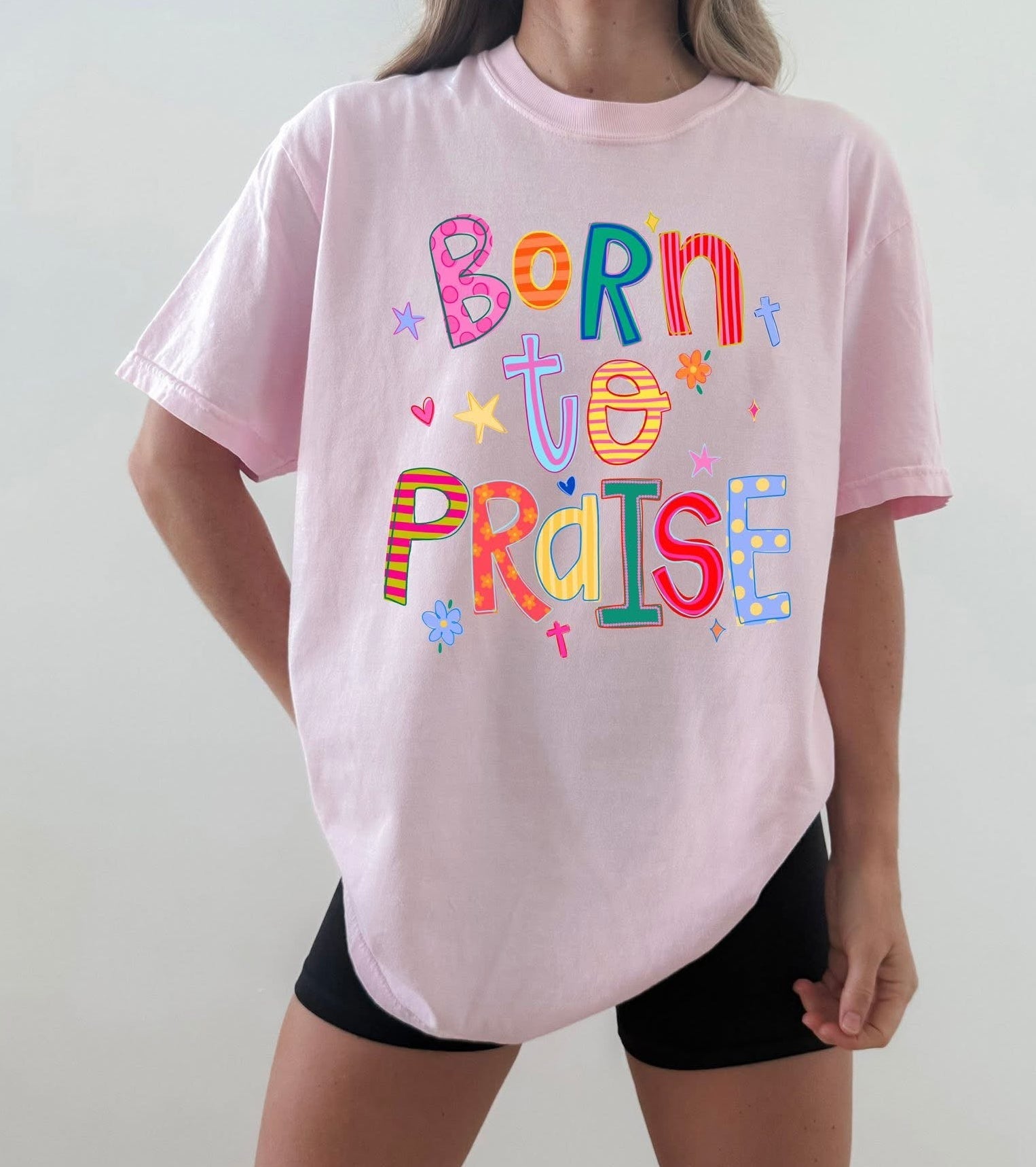 Person wearing a pink t-shirt with colorful text design on a plain background