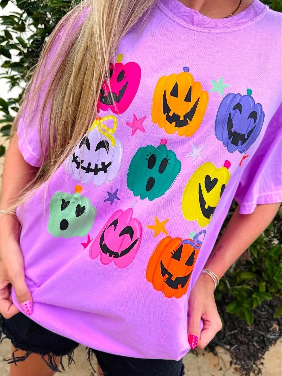 Person wearing a purple t-shirt with colorful pumpkin designs outdoors.