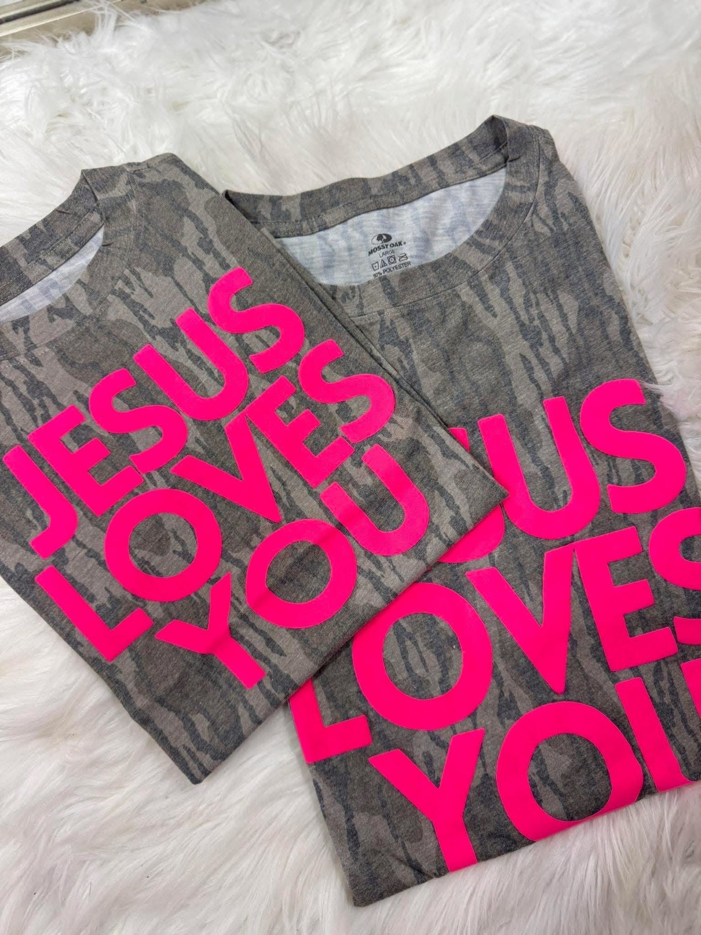Two folded shirts with 'Jesus Loves You' Puff neon vinyl text on a fluffy white surface
