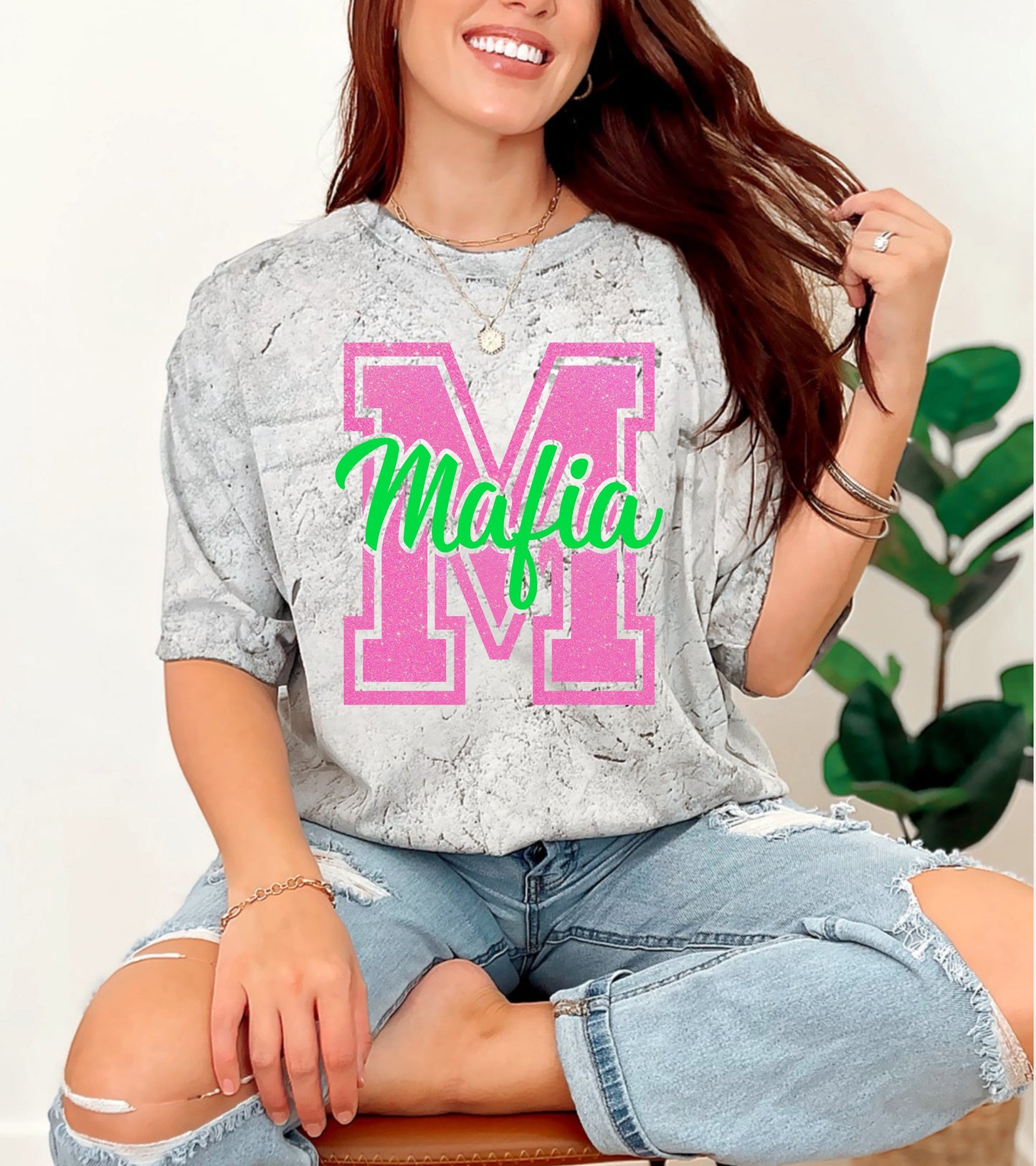 Woman wearing a gray oversized shirt with 'Mafia' print, sitting on a white background.