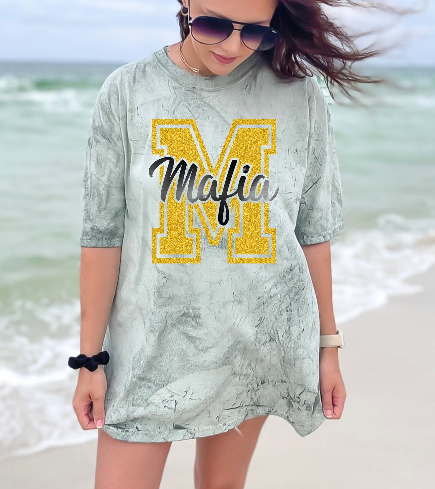 Woman wearing a gray dress with a yellow 'M' and the word 'Mafia' on a beach.