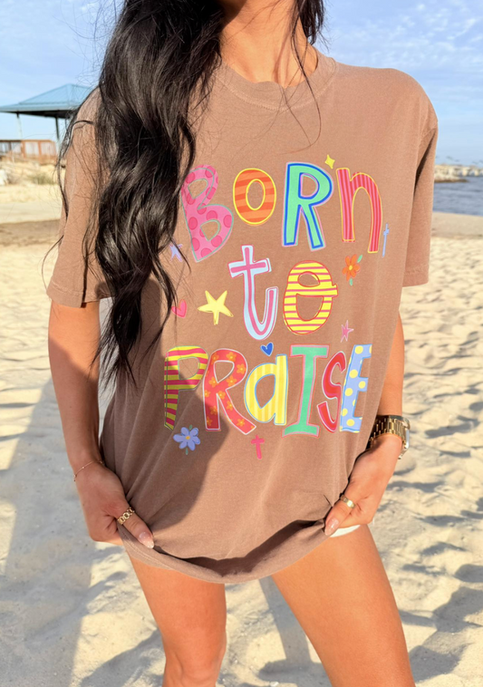 Woman wearing a brown t-shirt with 'Born to Praise' text on a beach