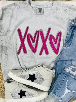 A Smoke Comfort Color t-shirt with pink 'XOXO' heart applique, paired with blue denim jeans and white sneakers with a star pattern.