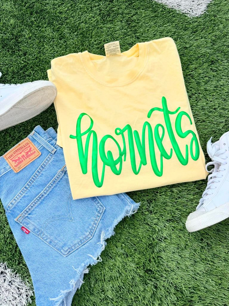 Yellow sweatshirt with 'hornets' text, blue jeans, and white sneakers on grass