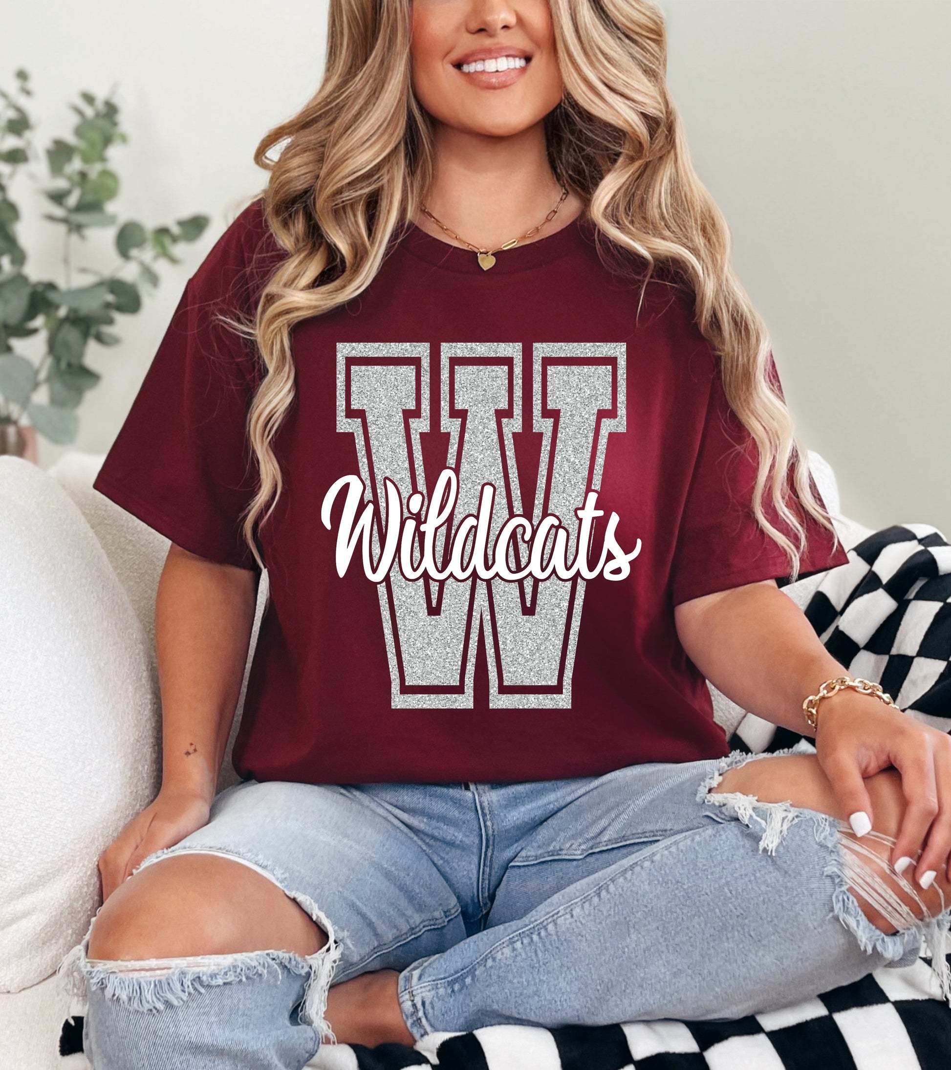 Person wearing a maroon t-shirt with 'Wildcats' printed on it, sitting on a checkered blanket.