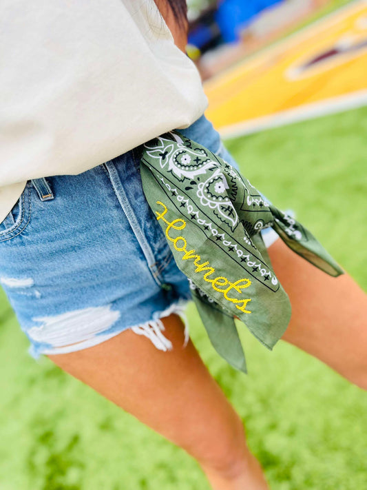 Person wearing denim shorts with a green bandana around their waist, featuring the word 'Hornets'.