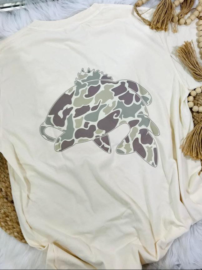 Ivory tee with a camouflage fish design on a rug surface.
