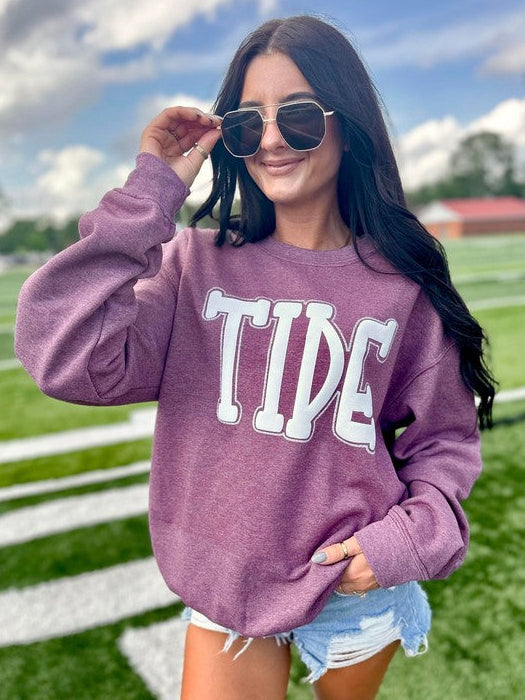 Woman wearing a purple 'TIDE' sweatshirt on a sports field