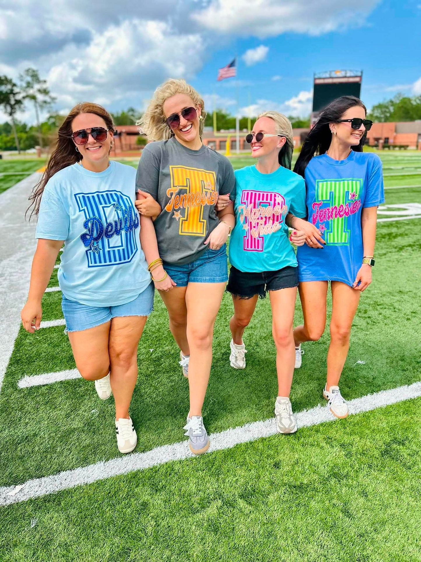 Four women walking on a football field wearing matching t-shirts with different designs.