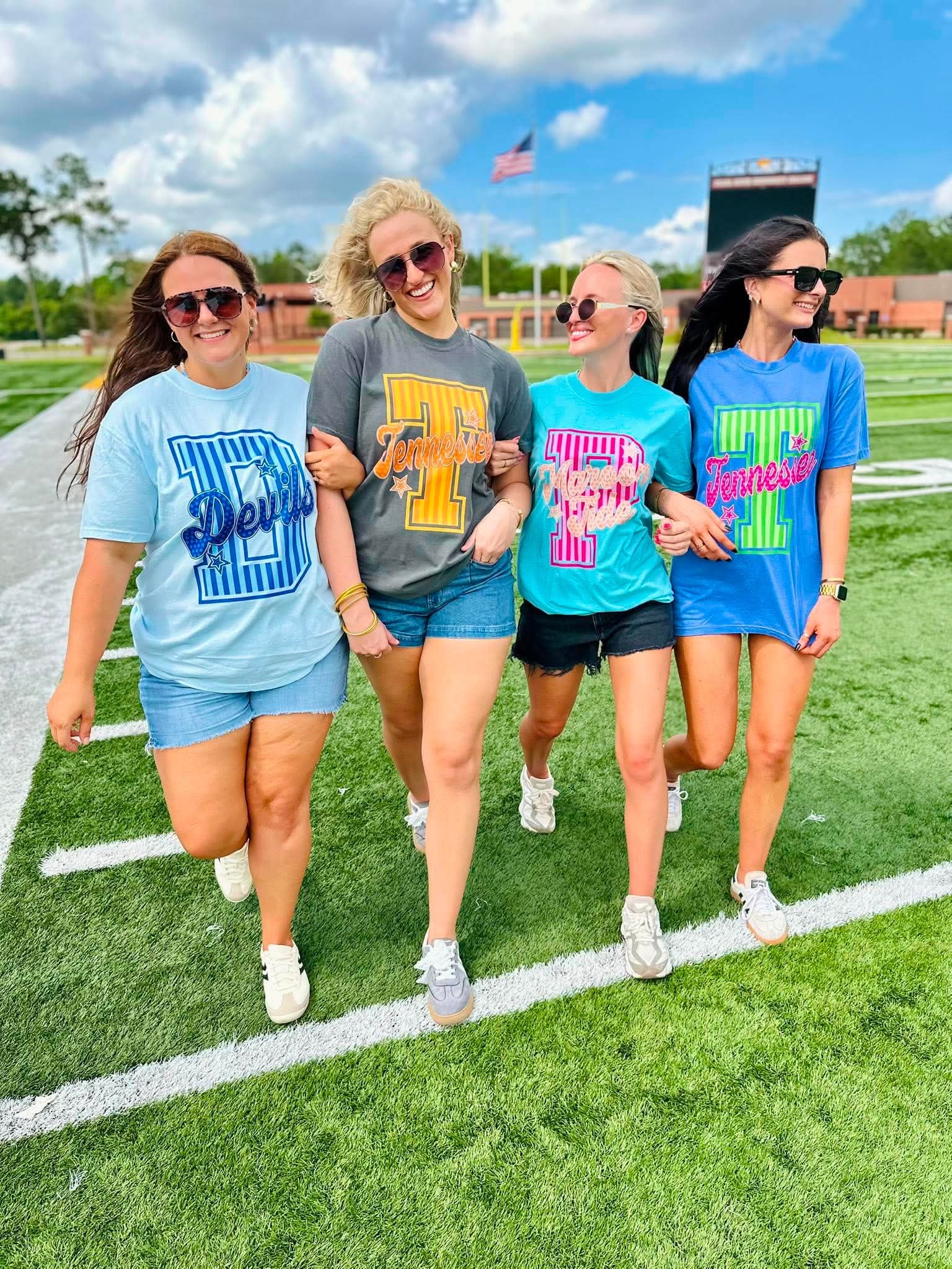 Four women walking on a football field wearing matching t-shirts with different designs.