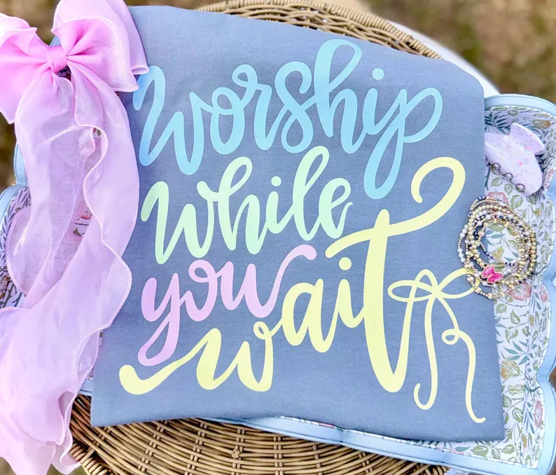 Decorative sign with 'Worship while you wait' text on a blue background, surrounded by decorative elements.