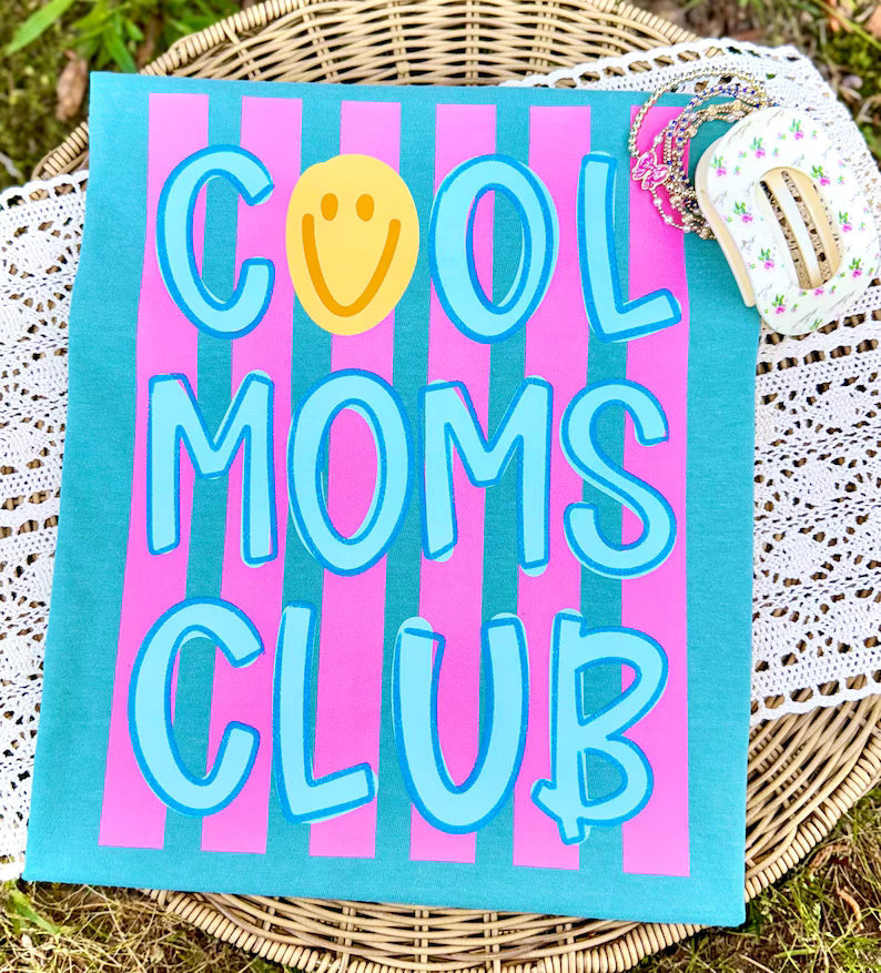 Canvas with 'Cool Moms Club' text on a striped background, placed on a woven surface.