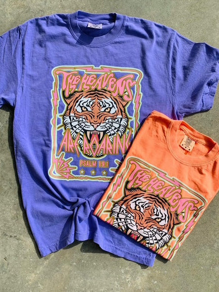 A graphic tee with a melon and violet color scheme featuring The Heavens Are Roaring Psalm 19:1 and a tiger design, laid flat on a surface.