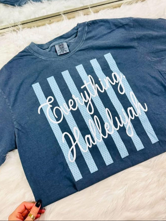 Blue t-shirt with 'Everything Hallelujah' text on a white surface