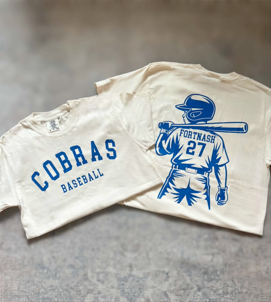 Two white t-shirts with blue graphics and text on a gray surface