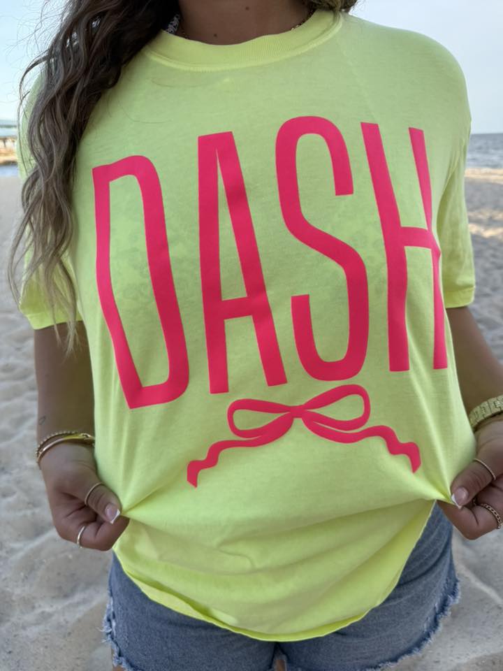 Person wearing a bright yellow t-shirt with 'DASH' printed in pink on a beach.