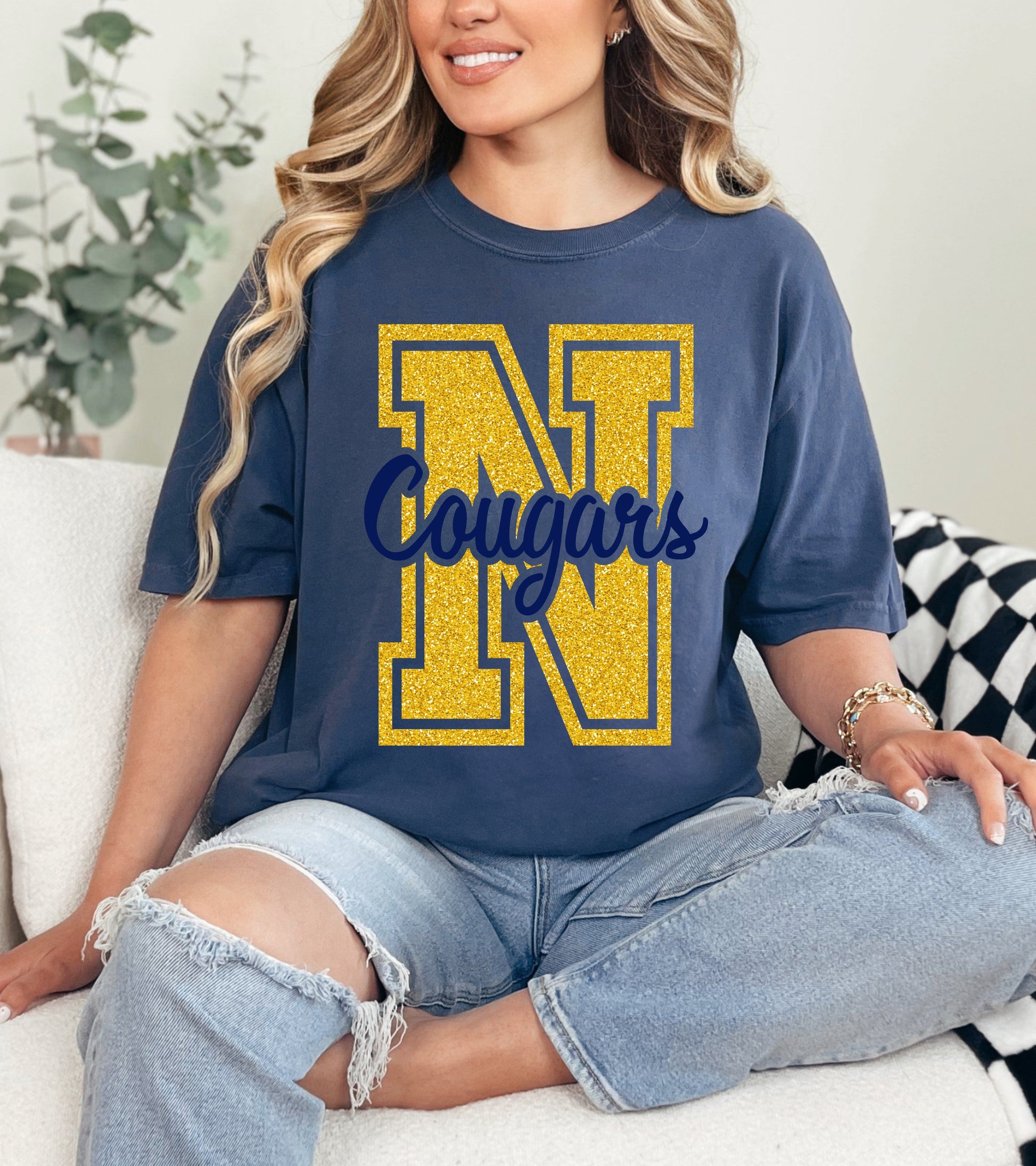 Woman wearing a blue t-shirt with 'N Cougars' design, sitting on a couch.